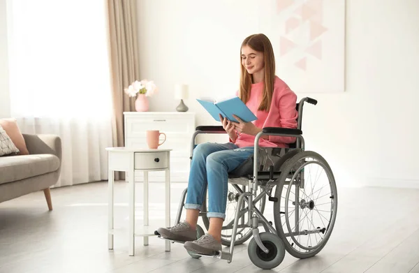 Tiener meisje met boek in rolstoel thuis — Stockfoto