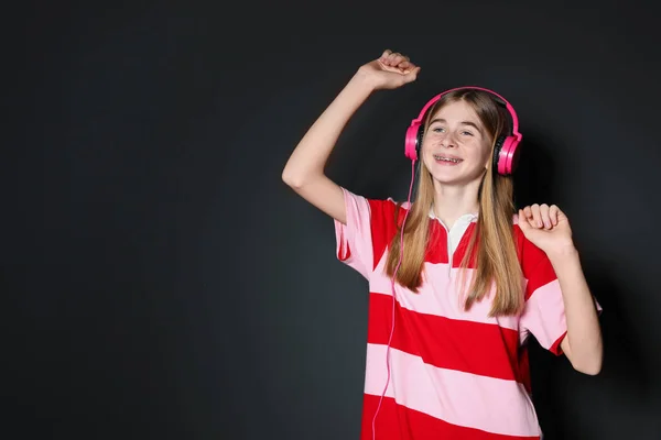 Adolescente disfrutando de la música en los auriculares sobre fondo negro. Espacio para texto —  Fotos de Stock