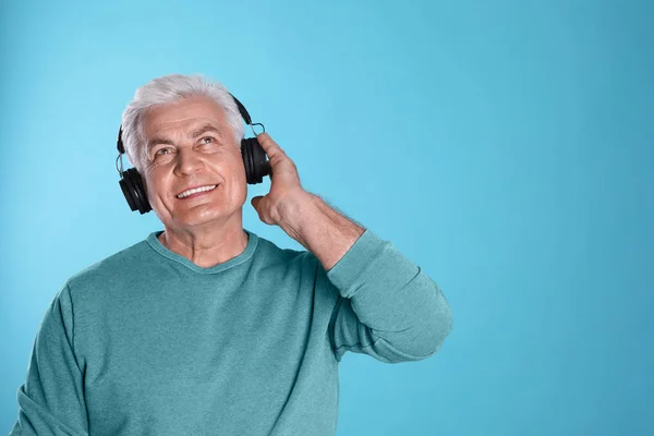 Hombre maduro disfrutando de la música en auriculares sobre fondo de color. Espacio para texto —  Fotos de Stock