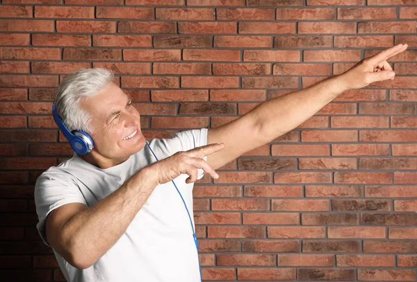 Зрелый мужчина наслаждается музыкой в наушниках против кирпичной стены — стоковое фото