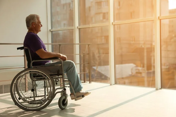 Ανώτερος άνθρωπος κάθεται σε αναπηρικό αμαξίδιο κοντά στο παράθυρο στο σπίτι — Φωτογραφία Αρχείου