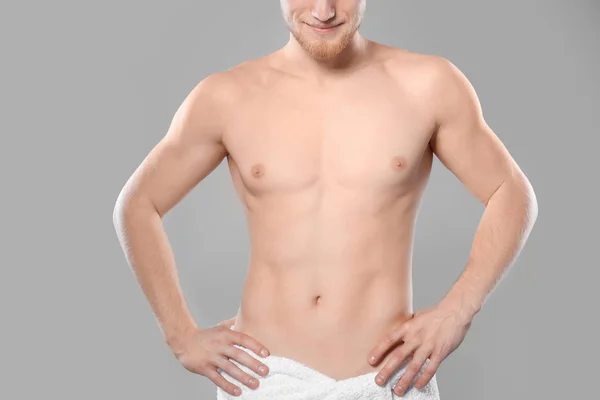 Młody mężczyzna z szczupłym ciałem w ręczniku na szarym tle, zbliżenie — Zdjęcie stockowe