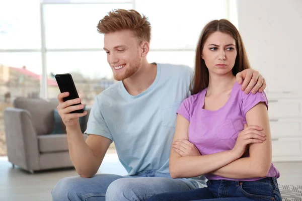 Jongeman die bezig is met smartphone terwijl hij tijd doorbrengt met zijn vriendin thuis. Eenzaamheid concept — Stockfoto