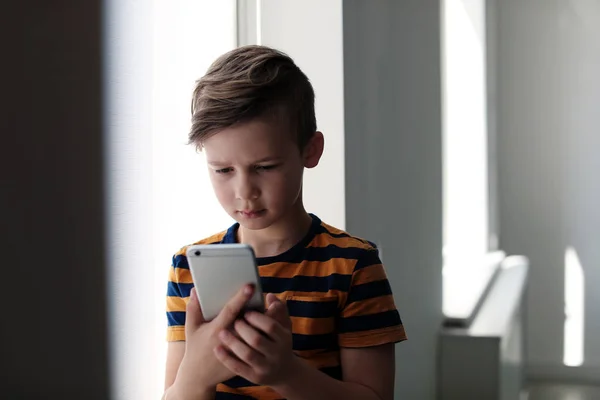 Сумна маленька дитина зі смартфоном у приміщенні. Небезпека Інтернету — стокове фото
