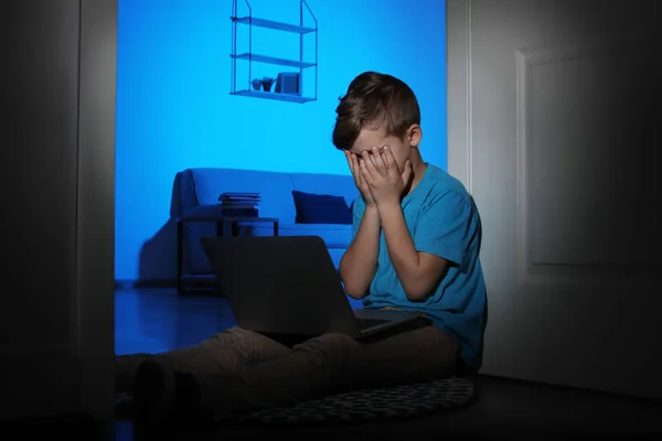 Frightened little child with laptop on floor in dark room. Danger of internet