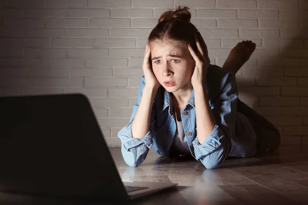 Menina adolescente chocada com laptop no chão no quarto escuro. Perigo da internet — Fotografia de Stock