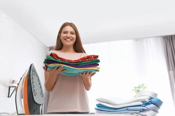 Jonge vrouw met gevouwen kleren in de buurt van strijkplank thuis. Ruimte voor tekst — Stockfoto