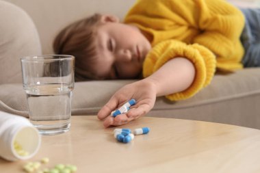 Evde kanepede hap ile bilinçsiz küçük çocuk. İlaç zehirlenmesinin tehlikesi