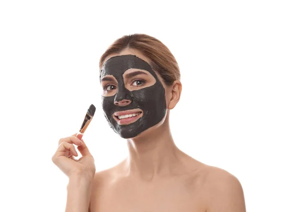 Beautiful woman applying black mask onto face against white background — Stock Photo, Image