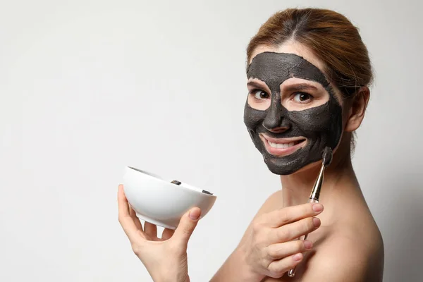 Beautiful woman applying black mask onto face against light background. Space for text — Stock Photo, Image