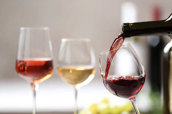 Pouring red wine from bottle into glass on blurred background. Space for text — Stock Photo, Image