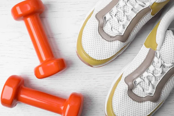 Dumbbells and sneakers on wooden background, flat lay — Stock Photo, Image