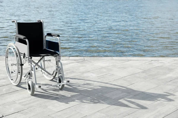 Empty wheelchair near river on sunny day. Space for text — Stock Photo, Image