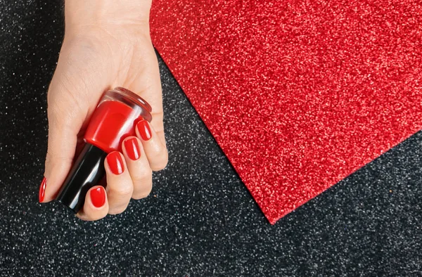 Mujer sosteniendo botella de esmalte de uñas rojo en mano cuidada sobre fondo de color, vista superior. Espacio para texto — Foto de Stock