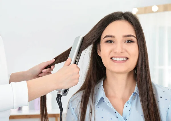 Frisör med modern plattång för att styla klientens hår i salongen — Stockfoto