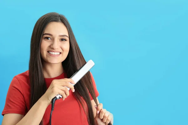 Jovem mulher usando ferro de cabelo no fundo azul, espaço para texto — Fotografia de Stock