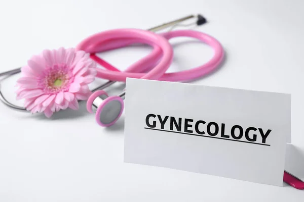 Kortti sanalla Gynekologia, leikepöytä, stetoskooppi ja kukka valkoisella taustalla — kuvapankkivalokuva