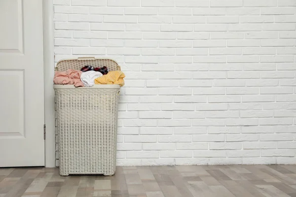 Пластиковая корзина с грязной одеждой у стены в комнате. Пространство для текста — стоковое фото