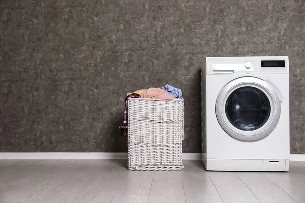 Плетеная корзина для белья, полная грязной одежды и стиральной машины возле цветной стены. Пространство для текста — стоковое фото