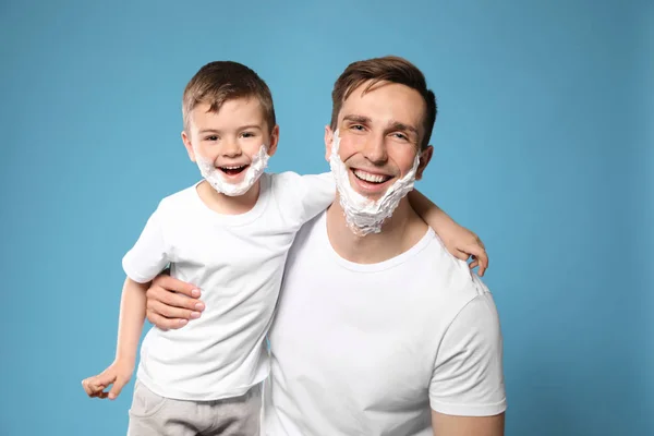 Vader en zijn kleine zoon met scheerschuim op gezichten tegen kleur achtergrond — Stockfoto