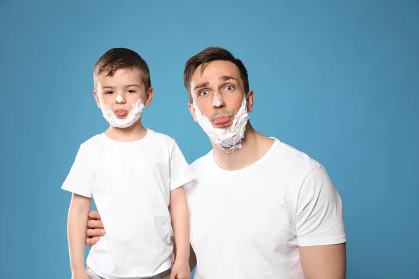 Drôle papa et son petit fils avec mousse à raser sur les visages sur fond de couleur — Photo