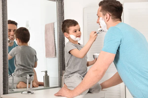 Kleiner Sohn sprüht Papa im Badezimmer Rasierschaum ins Gesicht — Stockfoto