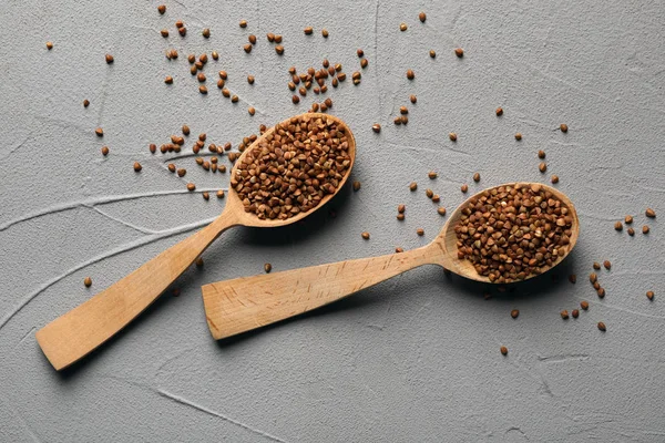 Cucharas de madera con trigo sarraceno sin cocer sobre fondo gris, puesta plana — Foto de Stock