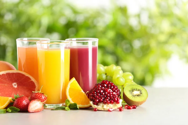 Три бокала с различными соками и свежими фруктами на столе на размытом фоне. Пространство для текста — стоковое фото
