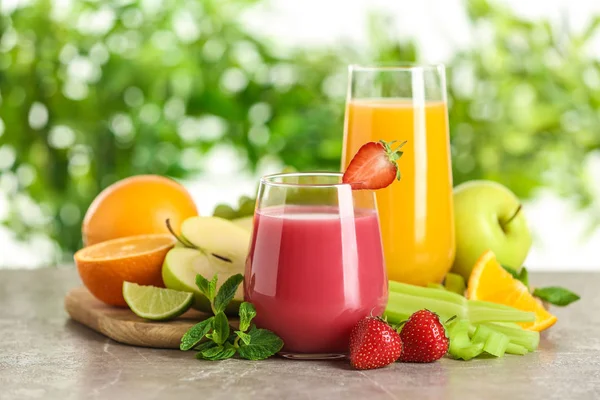 Glazen met verschillende sappen en vers fruit op tafel tegen onscherpe achtergrond — Stockfoto