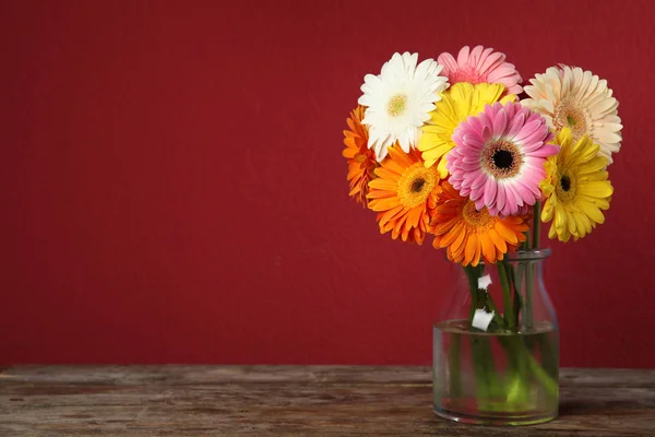 Csokor szép fényes Gerbera virágok vázában fából készült asztal ellen, színes háttér. Szóköz a szöveghez — Stock Fotó