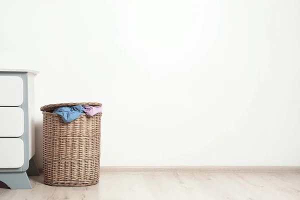 Wicker laundry basket with dirty clothes on floor near wall. Space for text — 스톡 사진