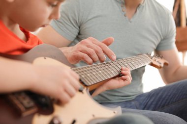 Küçük çocuk müzik dersinde öğretmeniyle gitar çalıyor, yakın çekim. Öğrenme notları