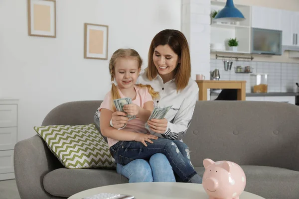 Mother and daughter counting money on sofa indoors