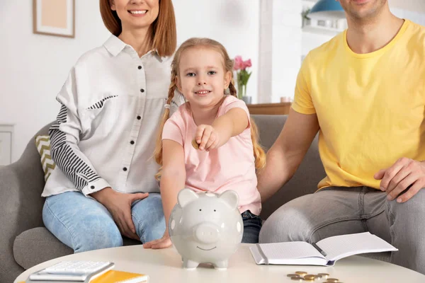 Familia feliz poniendo moneda en alcancía en la mesa en el interior. Ahorro de dinero —  Fotos de Stock