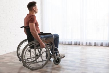 Evde pencere yakınında tekerlekli sandalyede oturan düşünceli adam