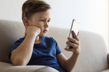Odada kanepede akıllı telefon olan küçük çocuk. İnternet tehlikesi