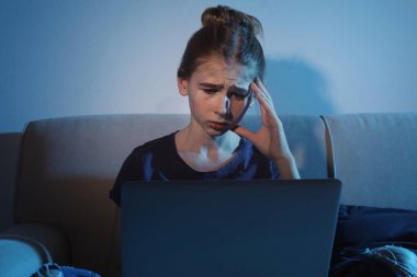 Karanlık odada kanepede dizüstü bilgisayar ile üzgün genç kız. İnternet tehlikesi
