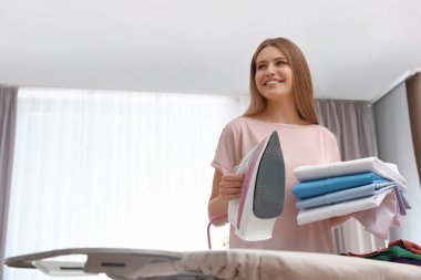 Evde katlanmış giysileri ve ütüsü olan genç bir kadın. Metin için boşluk