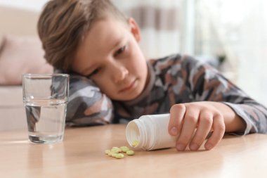 Masadaki hapları ve suyu olan küçük çocuk. İlaç zehirlenmesinin tehlikesi