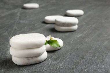 Gri masa üzerinde çiçek ve yaprakları ile yığılmış spa taşları. Metin için alan