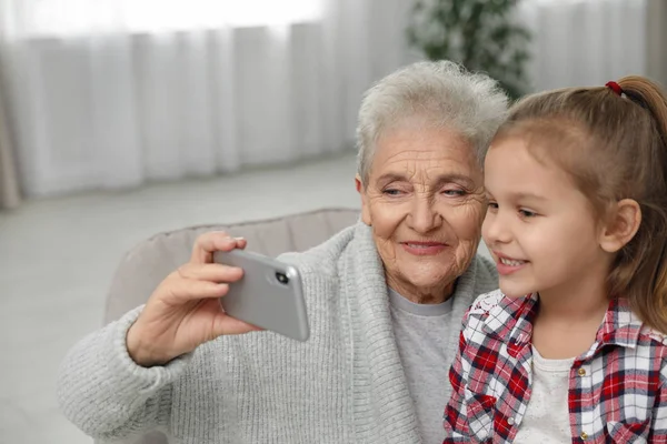 Menina bonito e sua avó tomando selfie em casa — Fotografia de Stock