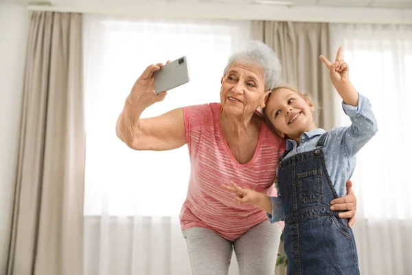 Menina bonito e sua avó tomando selfie em casa — Fotografia de Stock