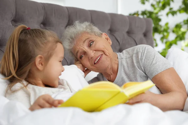 Fille mignonne et sa grand-mère lecture livre sur le lit à la maison — Photo