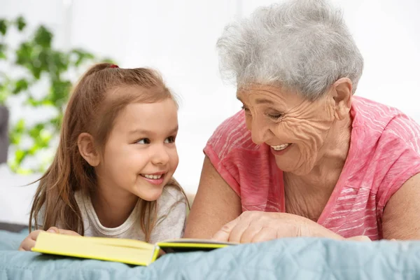 Menina bonito e sua avó ler livro na cama em casa — Fotografia de Stock
