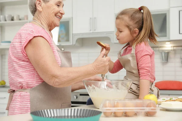 Cute girl and her grandmother cooking in kitchen