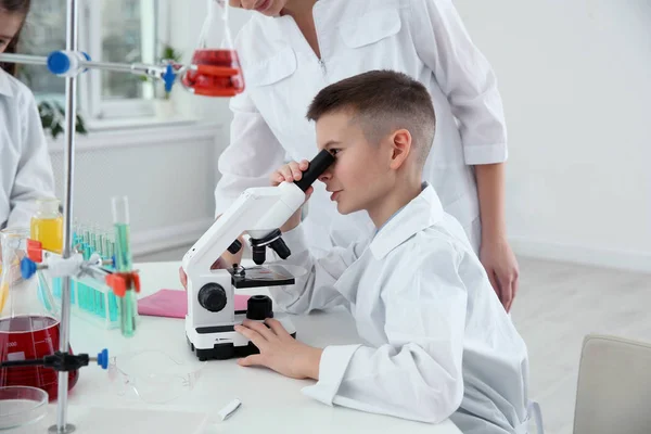 Colegial mirando a través del microscopio en la mesa en la clase de química — Foto de Stock