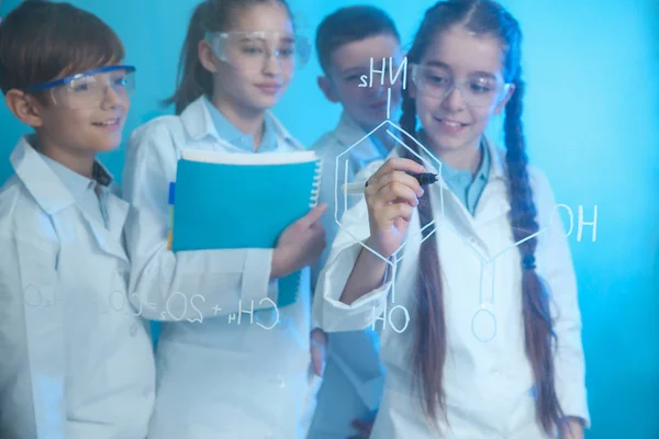 Ученики пишут формулу химии на стеклянной доске на цветном фоне — стоковое фото