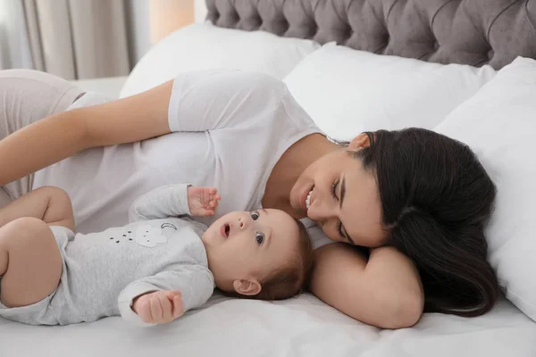 Portrait of mother with her cute baby lying on bed indoors — Stock Photo, Image