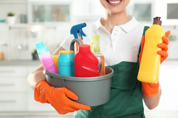 Mulher com bacia de detergentes e garrafa na cozinha, close-up. Serviço de limpeza — Fotografia de Stock