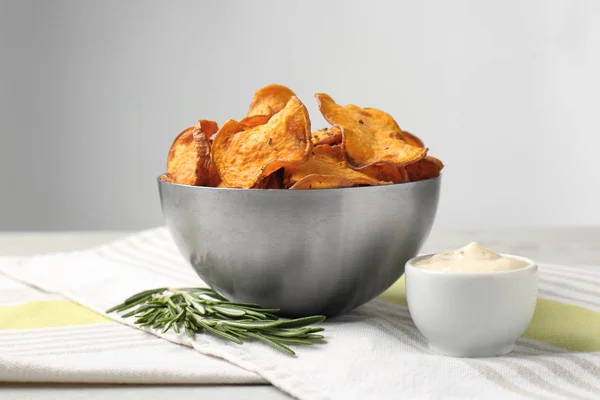 Bowl of sweet potato chips with sauce and rosemary on table against light background — Stock Photo, Image